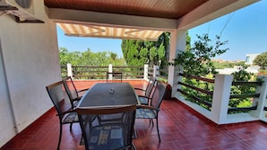 An outdoor patio with a round table and chairs, a wooden ceiling, and a view of greenery and buildings. - Apartment Rina- Two Bedroom Apartment with Terrace (Mandre)