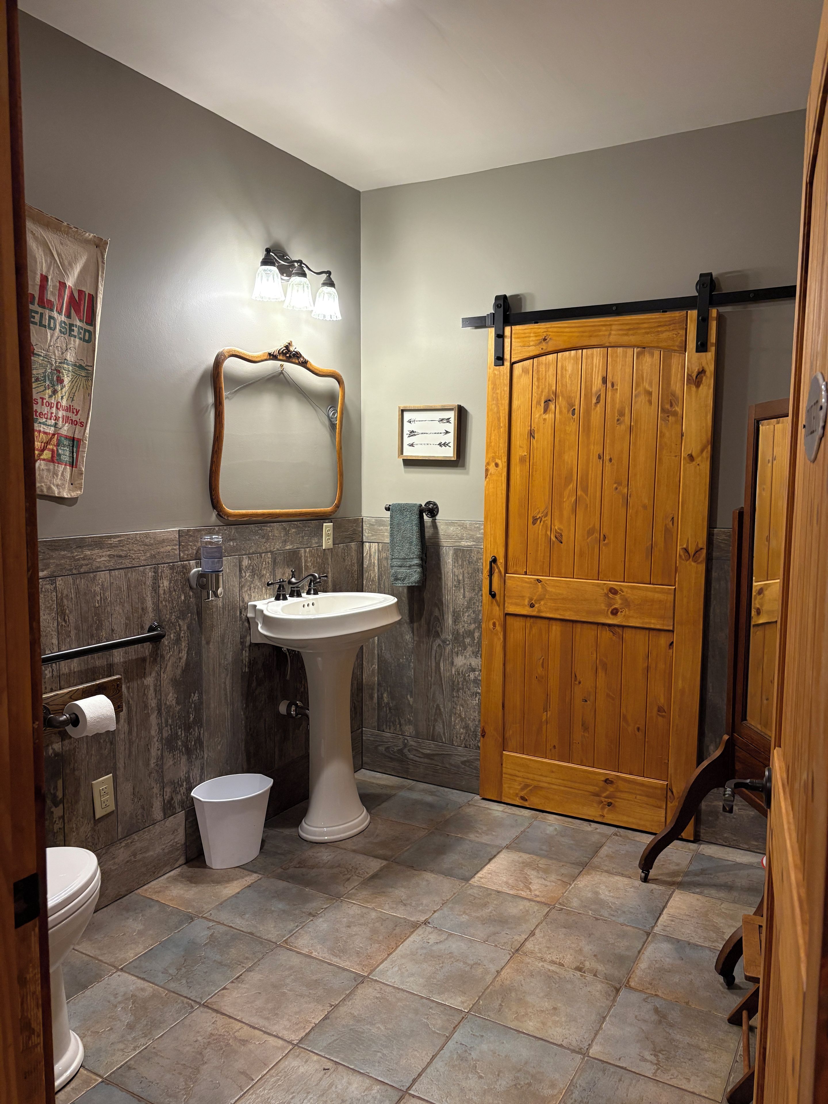 A bathroom with a wooden door, a sink, a mirror, and a towel rack.