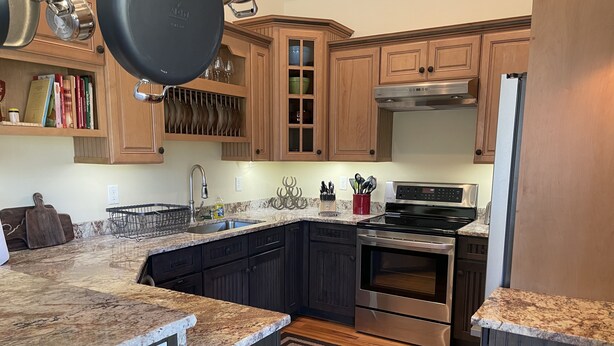 A kitchen with dark wood cabinets, granite countertops, stainless steel appliances, and a dish rack.