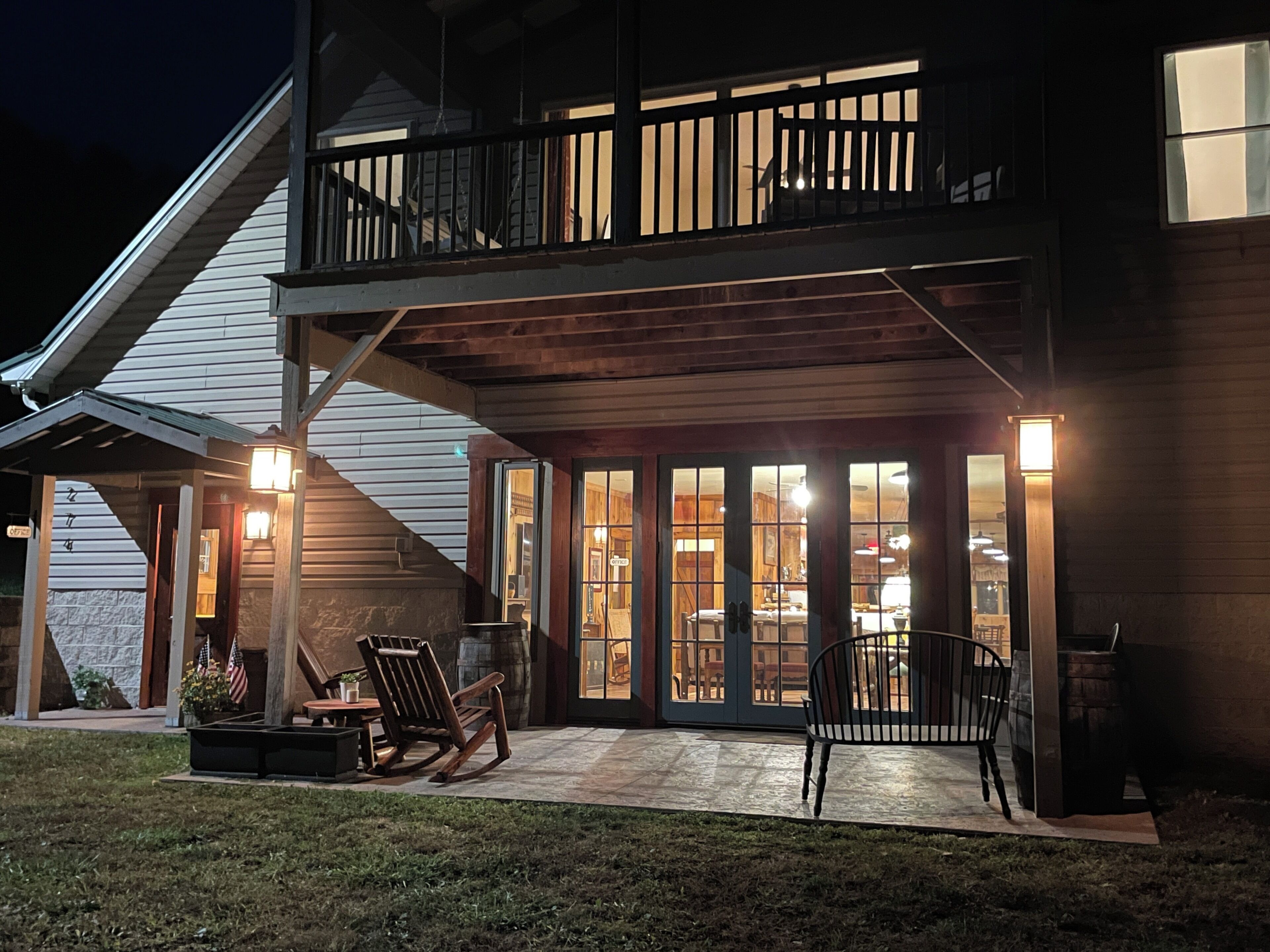 A two-story house with a covered patio, outdoor seating, and a visible interior through glass doors.