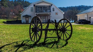 A large house with a balcony, a carriage in front, and a forested hill in the background.