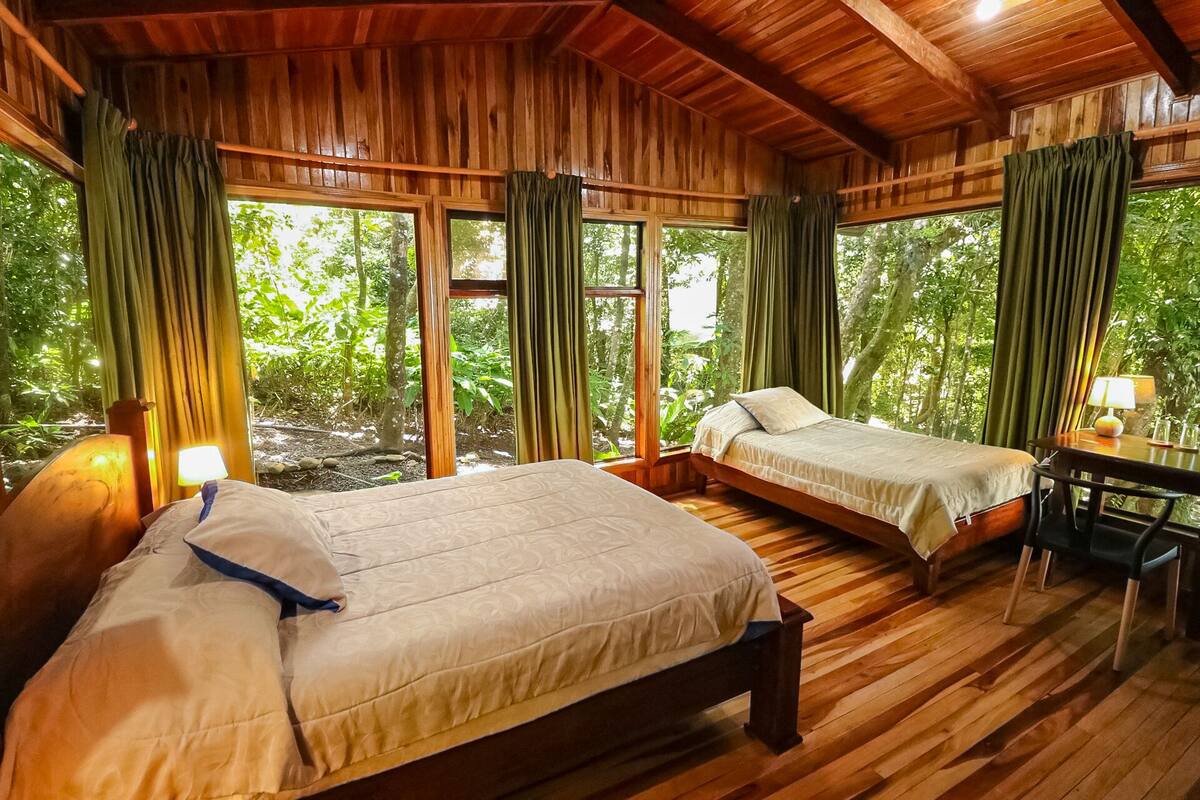 A wooden cabin with two beds, a desk, and a lamp.