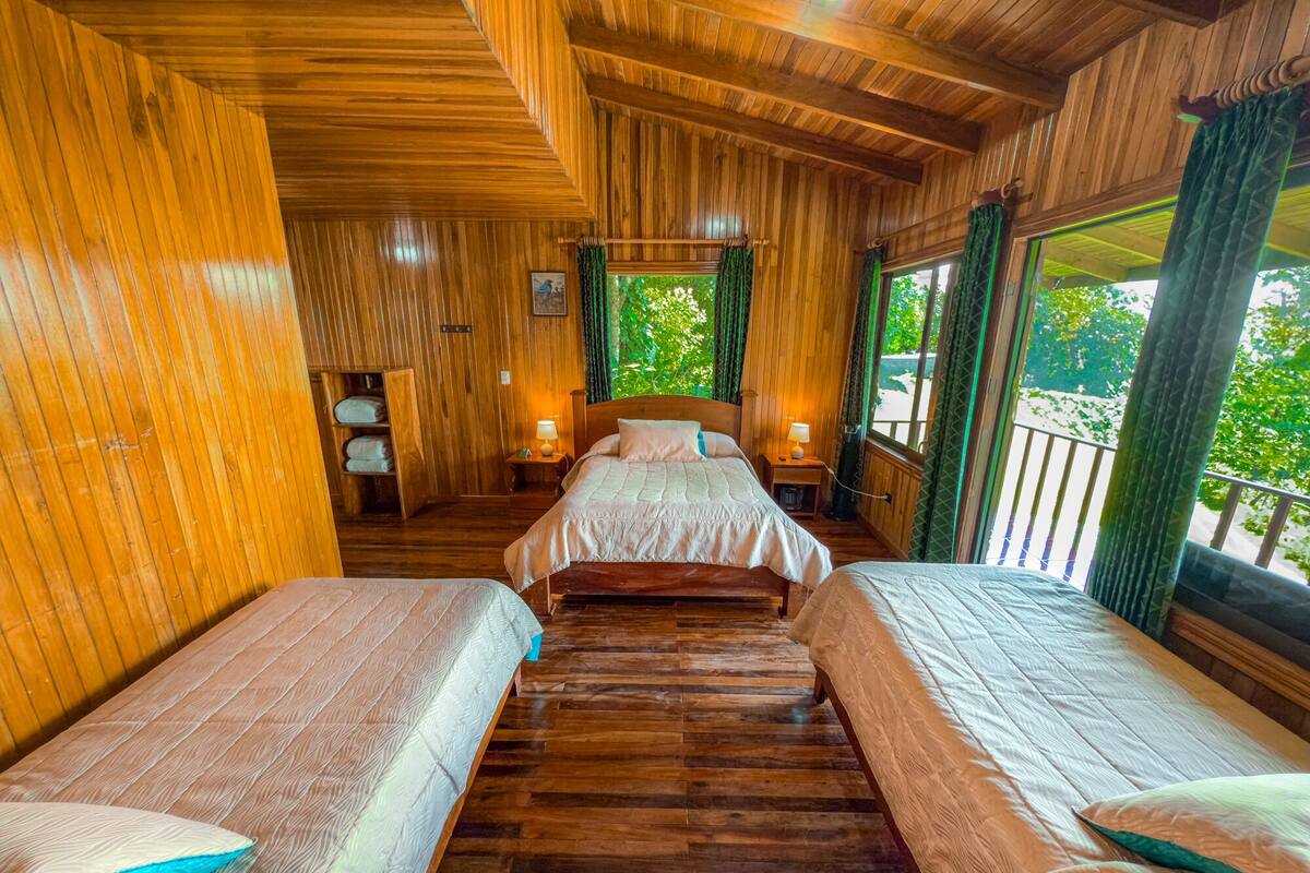 A wooden room with two beds, a nightstand, and a window with curtains.