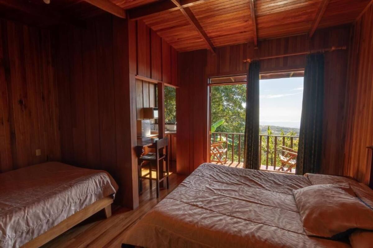 A wooden cabin with two beds, a desk, and a balcony with a view.
