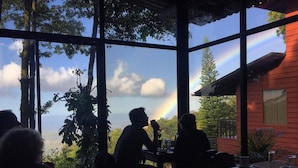 A dining area with large windows overlooking a scenic landscape, including a rainbow. - Hotel Flor de Bromelia (Monteverde)