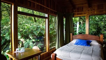 Una stanza in legno con un letto, un tavolo e ampie finestre su un rigoglioso giardino.