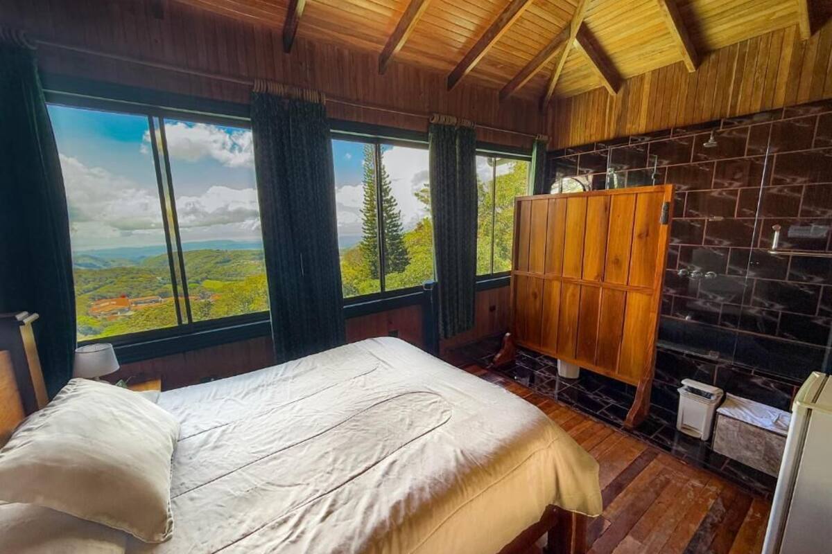 A bedroom with a large window, wooden ceiling, and a stone wall.