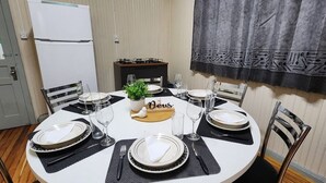 Une table à manger dressée pour quatre personnes, avec des assiettes blanches, des sets de table noirs et un centre de table composé d’une plante et d’un bloc de bois sur lequel est inscrit le mot « Deus ».