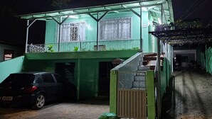 Un immeuble de deux étages à la façade verdoyante, avec une voiture garée devant et une ruelle étroite à côté.