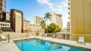 A swimming pool with lounge chairs and a view of surrounding buildings. - Marine Surf by Luana HI Vacation Rental (Honolulu)