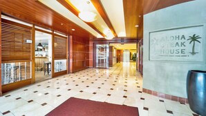 A hotel lobby with a checkered floor, wooden paneling, and a sign for Aloha Steak House. - Marine Surf by Luana HI Vacation Rental (Honolulu)