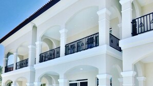 A hotel with a pool, outdoor seating, and a multi-level balcony with black railings. - Ocean view house with pool & BBQ (Noord)