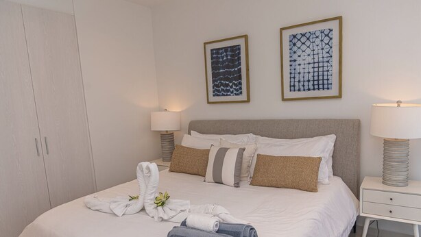 A neatly made bed with towels and a flower, a bedside table with a lamp, and two framed artworks on the wall. - Ocean view house with pool & BBQ (Noord)