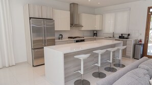 A modern kitchen with a central island, stainless steel appliances, and bar stools. - Ocean view house with pool & BBQ (Noord)
