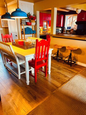A dining area with a wooden table, red chairs, and a kitchen in the background. - Beachside Two Bedroom Condo with Private Hot Tub (Homer)