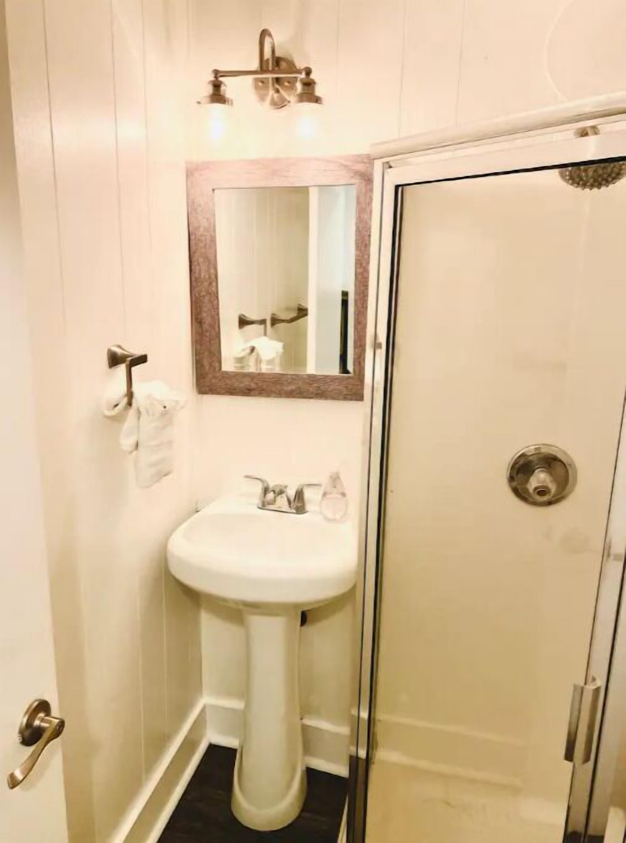 A bathroom with a pedestal sink, a mirror, a towel rack, and a glass shower enclosure.