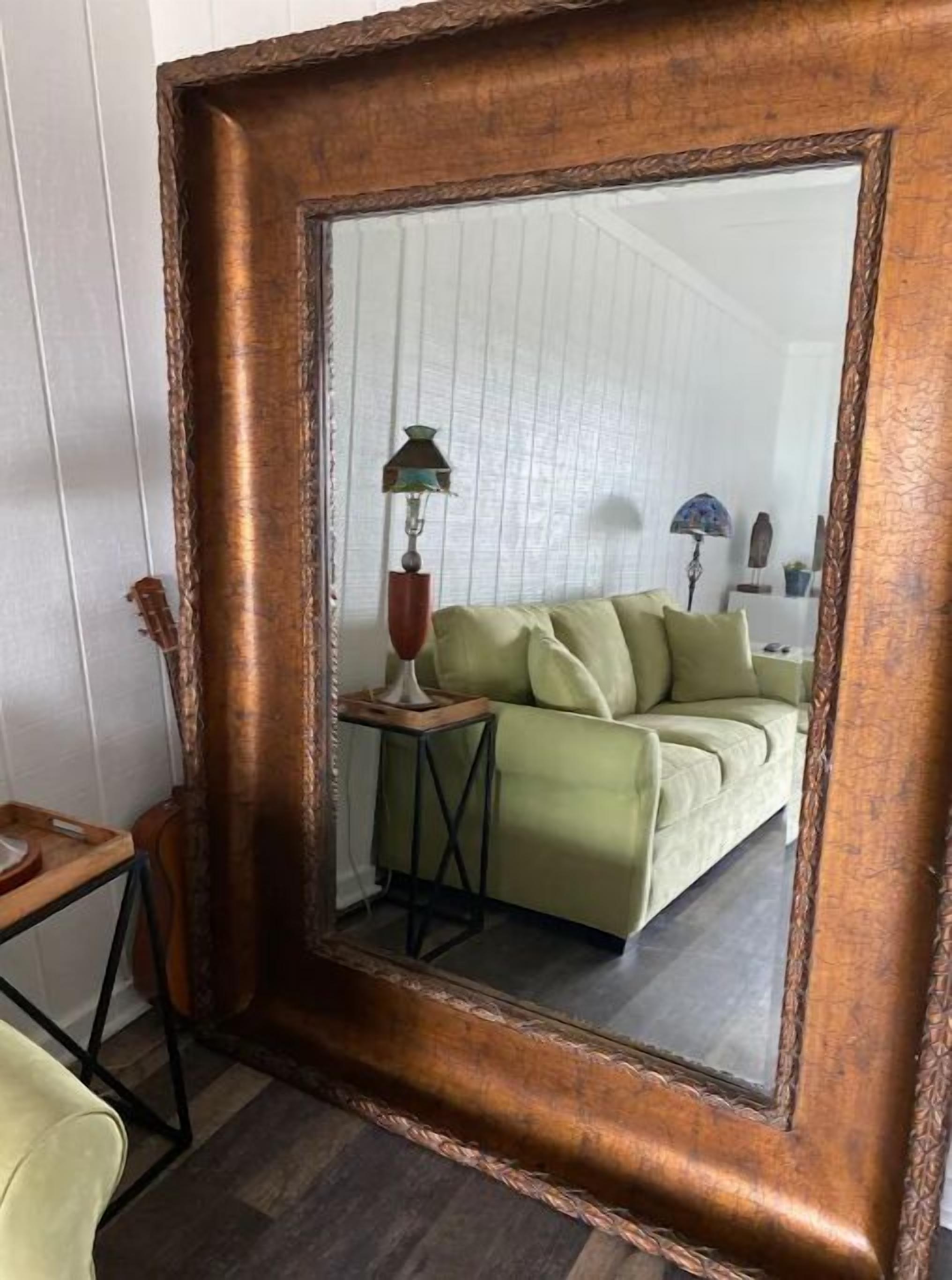 Un espejo con marco de madera refleja una habitación con un sofá verde, una lámpara y una pequeña mesa.