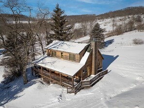 Eine Blockhütte mit verschneitem Dach, einer Holzdielen-Terrasse und einem Schornstein.