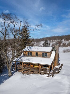 Une cabane en bois avec un toit enneigé, une terrasse et une cheminée.