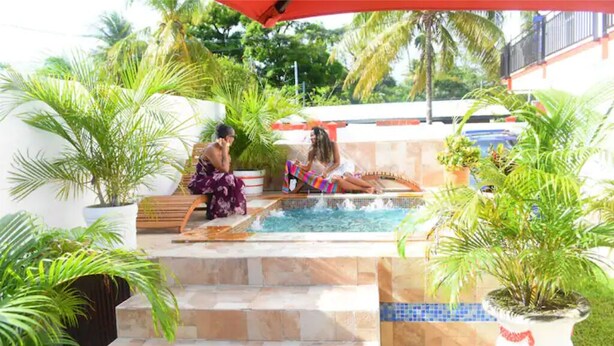 A pool area with steps leading to a hot tub, surrounded by potted plants and palm trees. - 1, Bedroom Suites, of Leisure and SPA (Mayaro)