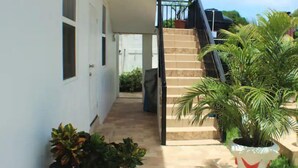 A pathway leading to a staircase, flanked by potted plants and a white pot with a red design. - 1, Bedroom Suites, of Leisure and SPA (Mayaro)