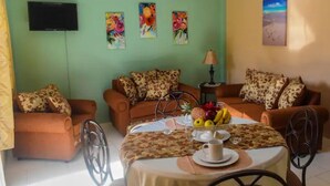 A living room with two sofas, a coffee table with fruit and a cup, and a TV on the wall. - 1, Bedroom Suites, of Leisure and SPA (Mayaro)