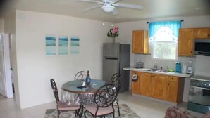 A compact kitchen with a refrigerator, stove, and wooden cabinets. A dining table with chairs is in the center, surrounded by a patterned rug. - 1, Bedroom Suites, of Leisure and SPA (Mayaro)
