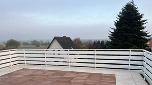 A wooden deck with white railings, overlooking a rural landscape with houses and trees. - A modern renovated apartment with balcony terrace. (Lübbecke)