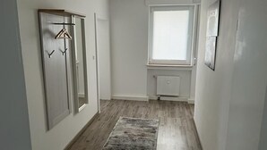 A narrow hallway with wooden flooring, a radiator, and a window with blinds. - A modern renovated apartment with balcony terrace. (Lübbecke)
