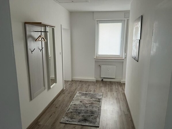 Een smalle gang met houten vloer, een radiator en een raam met jaloezieën.