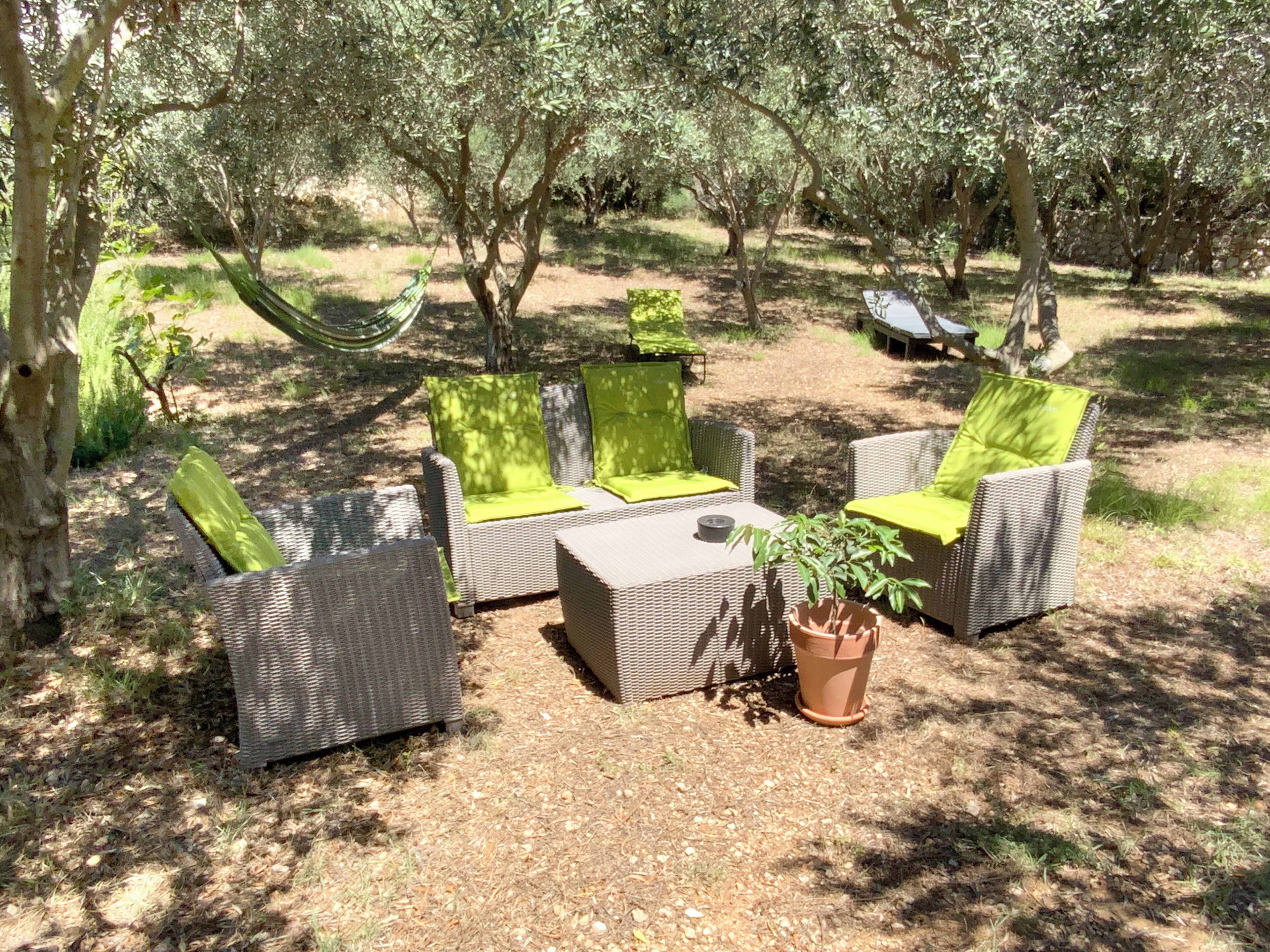 An outdoor seating area with wicker furniture and green cushions, surrounded by trees and a hammock.