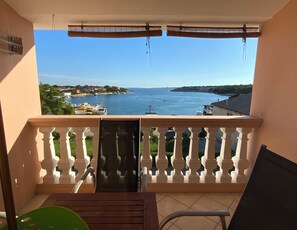 A balcony with a view of the sea, a chair, a table, and a window with blinds. - Olive House (Pag)