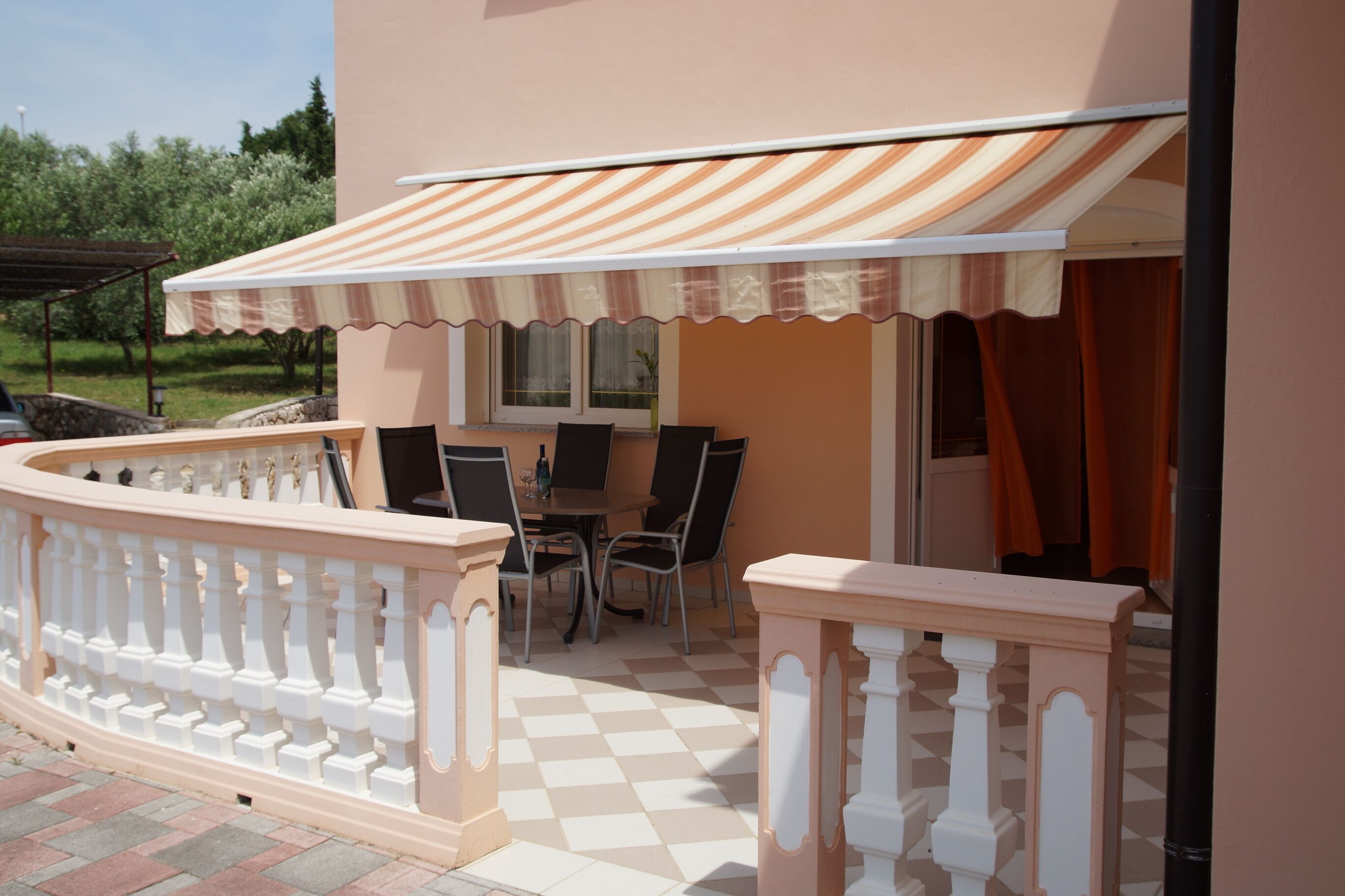 An outdoor patio with a checkered floor, a table with chairs, and a striped awning.