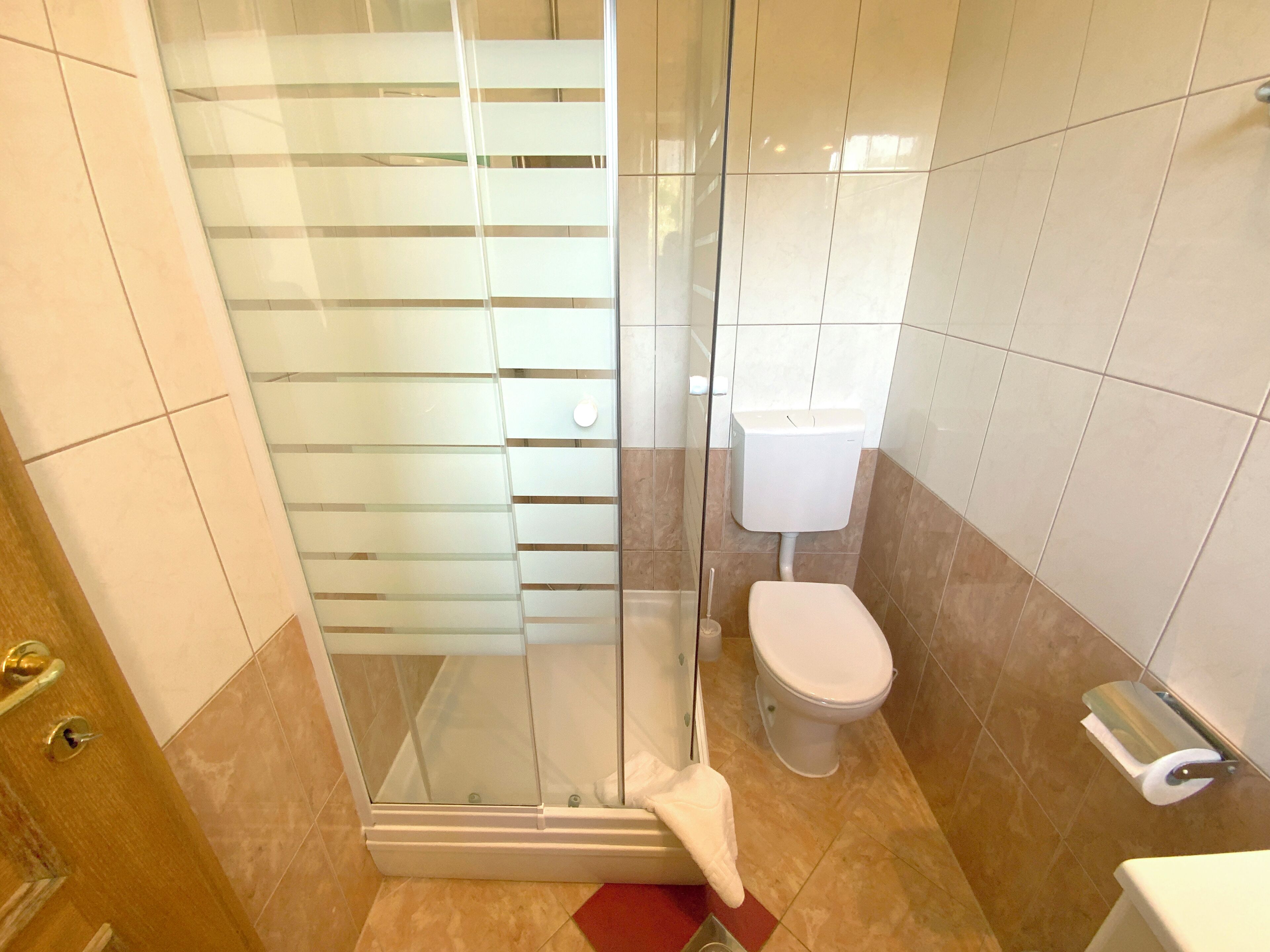 A bathroom with a glass shower enclosure, a toilet, and a hand dryer.