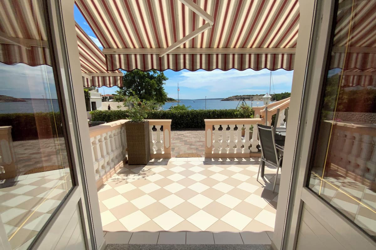 An outdoor patio with a checkered floor, a white balustrade, and a view of the sea.