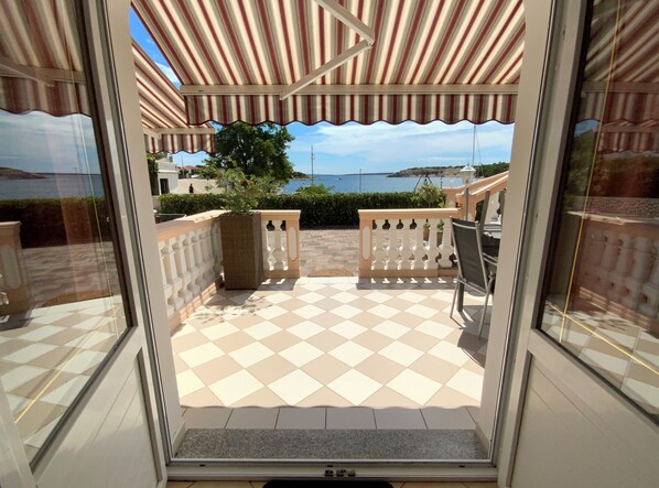 An outdoor patio with a checkered floor, a white balustrade, and a view of the sea. - Olive House (Pag)