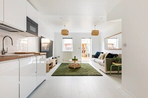 A modern kitchen with white cabinets, a wooden countertop, and a built-in oven. There is a green rug in the center of the room, and a small round table with a plant. - Family King Suites with Free Parking & Garden (London)