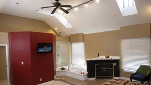 Un salon spacieux doté d’une grande fenêtre, d’une cheminée, d’un mur d’accent rouge et d’un ventilateur de plafond.