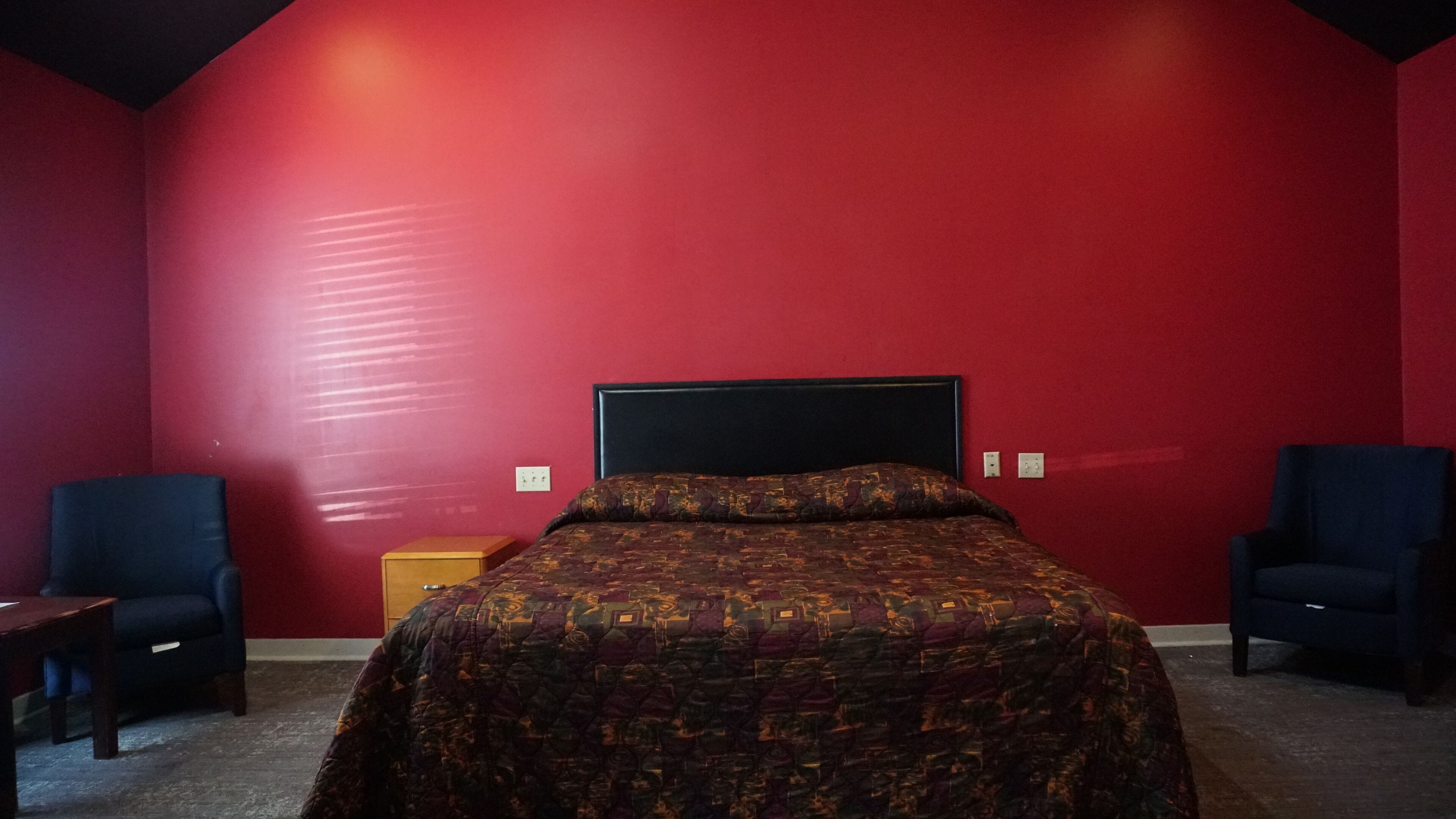 A room with a large bed, two armchairs, a small wooden cabinet, and red walls.