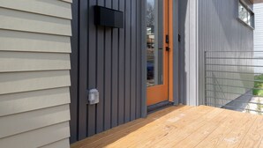 A modern building with a combination of siding and vertical panels, a wooden deck, and a door with a glass panel. - Modernist Masterpiece: 'Simply the Best' (Durham)