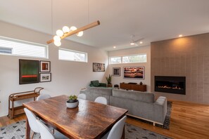Una sala de estar moderna con una mesa de comedor de madera, un sofá gris y una chimenea.