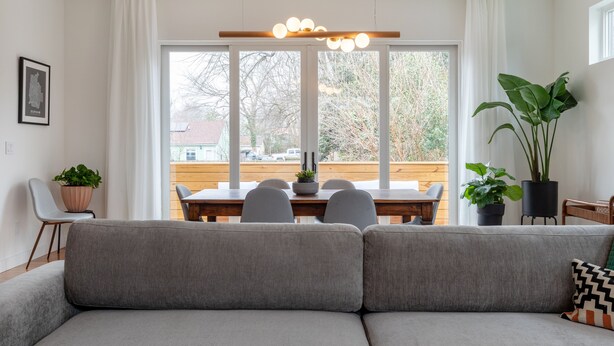 A modern living room with a grey sofa, a dining table with chairs, and a large window with curtains. - Modernist Masterpiece: 'Simply the Best' (Durham)