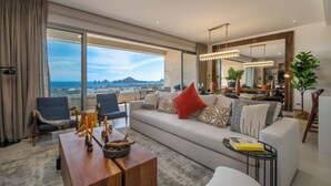 A modern living room with a large window, a sofa, a coffee table, and a dining area. - Stunning New Luxury Condo with Breathtaking Ocean Views (El tezal)