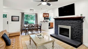 Un salon moderne avec une cheminée, un coin repas et une cuisine en arrière-plan.
