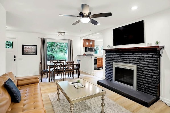 A modern living room with a sofa, coffee table, fireplace, and dining area.