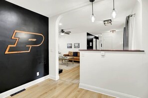 Un espace de vie moderne avec un mur noir orné d’une grande lettre « P », un plancher en bois, un coin cuisine avec un comptoir et un ventilateur de plafond.