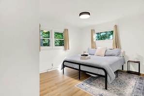 A bedroom with a bed, windows, a nightstand, and a rug.