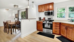 A modern kitchen with wooden cabinets, stainless steel appliances, and a dining area with a table and chairs. - Boiler Bungalow - entire 3(King)Bed home! (West Lafayette)