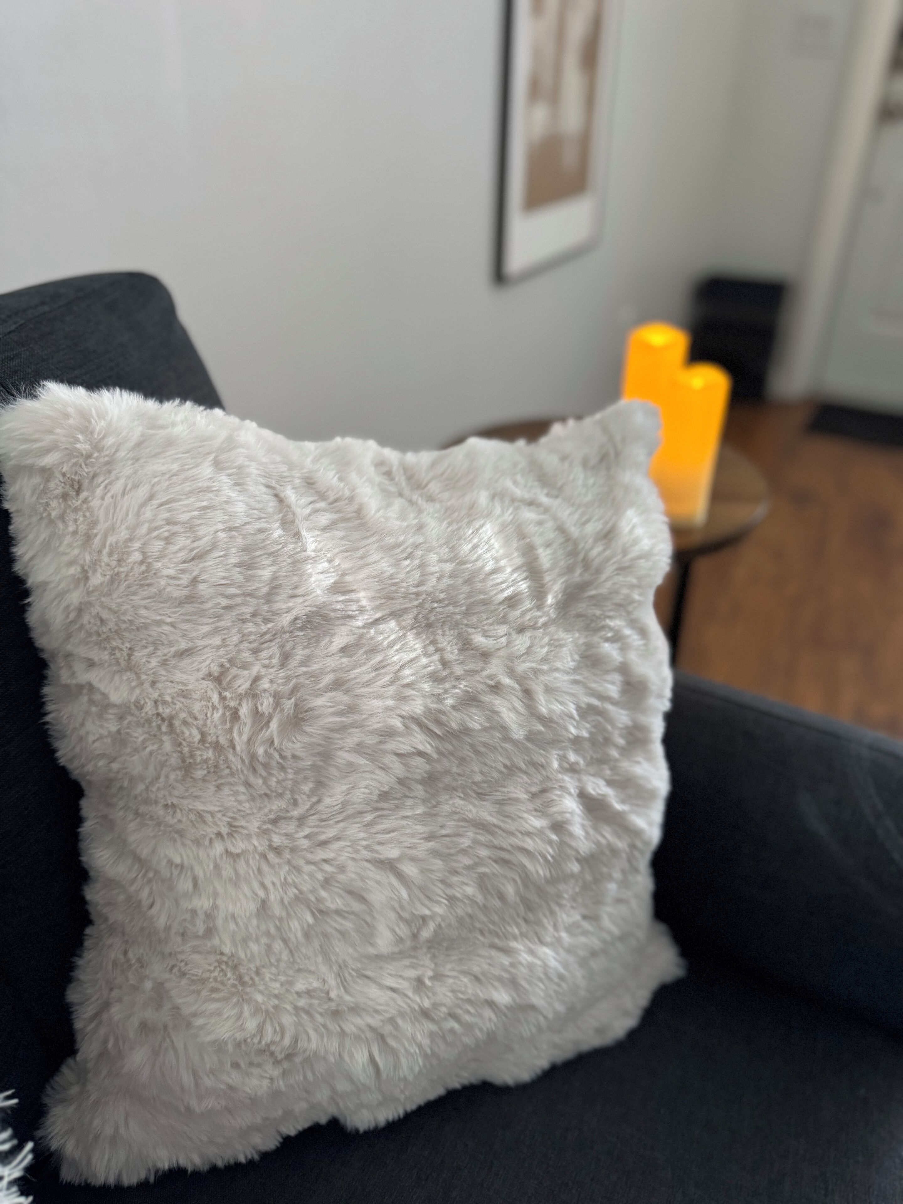 A plush, light-colored throw pillow on a dark sofa.