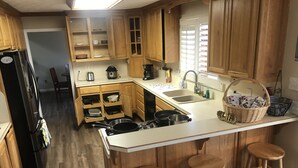 A compact kitchen with wooden cabinets, a built-in stove, a sink, and a refrigerator. There are three stools at the counter.